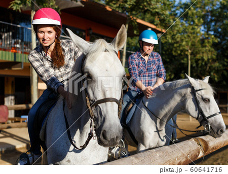 Mature couple in helmets riding by horse at barn at summer day Mature couple in helmets riding by horse at barn at summer day 60641716