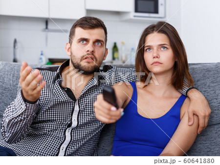 Young couple with TV remote sitting at sofa watching movie 60641880
