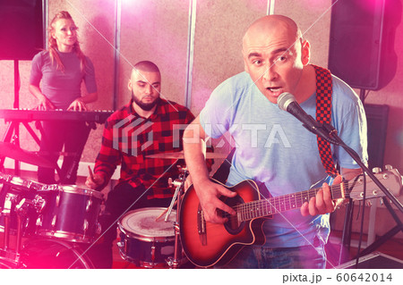 Rehearsal of music group. Band leader playing guitar and singing 60642014