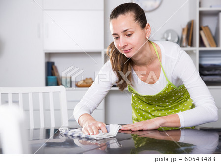 Young woman in an apron cleans the table at home 60643483
