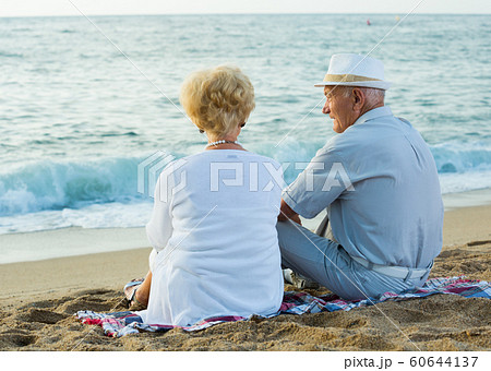 Mature man and woman sitting back on towel Mature man and woman sitting back on towel 60644137