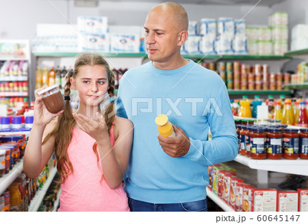 Girl with father looking different goods in supermarket Girl with father looking different goods in supermarket 60645147