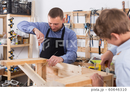 teacher and boy chiselling a wooden bench in workshop 60646310