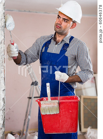 adult attentive man repairer working with roller in uniform, gloves and helmet adult attentive man repairer working with roller in uniform, gloves and helmet 60646378