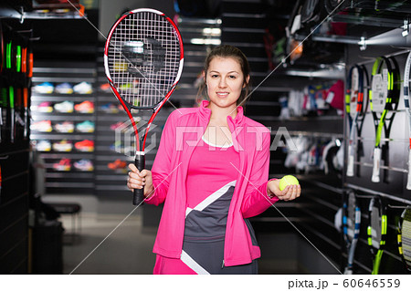 Sporty female is demonstraiting new rocket and ball for tennis in the store. 60646559