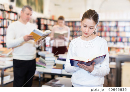 Portrait of intelligent preteen girl browsing textbooks in public library 60646636
