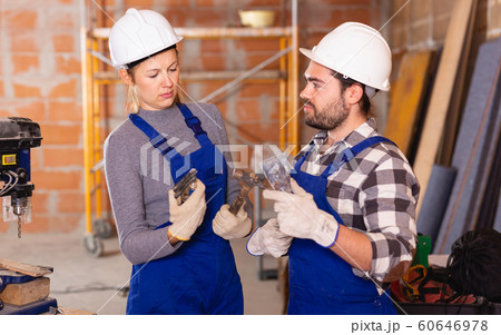 Portrait of two confident workers in uniform with tools inside brick cottage Portrait of two confident workers in uniform with tools inside brick cottage 60646978