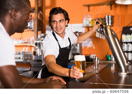Positive man bartender giving glass of golden beer to man client 60647506