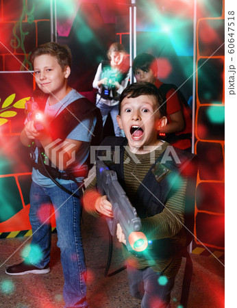 Emotional teen boy with laser pistol playing laser tag with frie 60647518