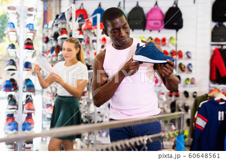 Afro man trying sneakers with help of female shop assistant in s Afro man trying sneakers with help of female shop assistant in s 60648561