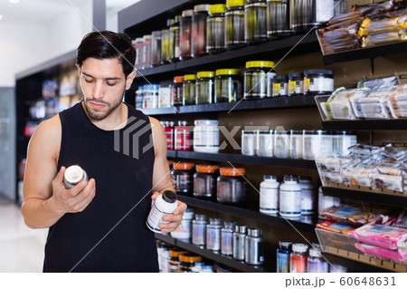 Serious young muscular man choosing sport nutrition products in shop Serious young muscular man choosing sport nutrition products in shop 60648631