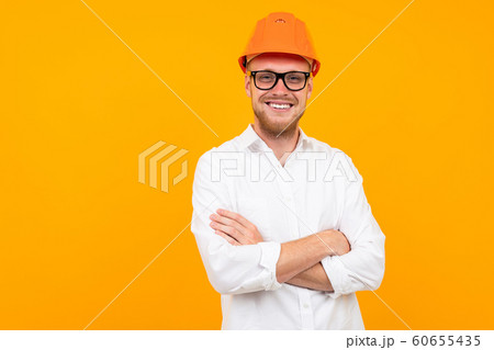 Beautiful caucasian engineer man with glasses and orange helmet isolated on yellow background Beautiful caucasian engineer man with glasses and orange helmet isolated on yellow background 60655435