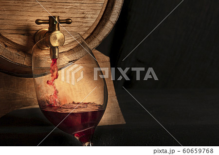 Pouring wine panoramic shot, a design template with copy space. A wineglass filled from an oak barrel, a closeup on a dark background with a place for text Pouring wine panoramic shot, a design template with copy space. A wineglass filled from an oak barrel, a closeup on a dark background with a place for text 60659768