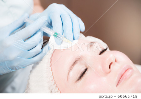 Close-up Attractive young woman gets anti-aging face injections. She lies calmly in a clinic or salon. An experienced young cosmetologist fills female wrinkles with hyaluronic acid from a syringe 60665718