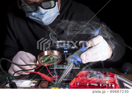 An engineer is looking for a breakdown in a broken computer with a magnifying glass. 60667230