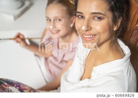 Cheerful young daughter with painted nose posing for camera with her mother 60669826