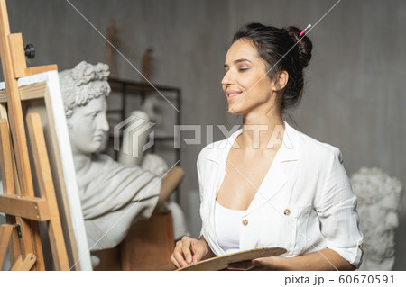 Charming young female artist admiring a picture near easel 60670591