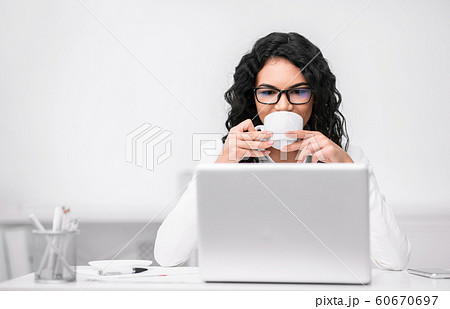 Latin woman drinking coffee and looking at laptop 60670697