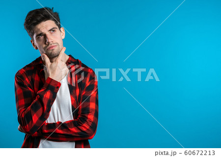 Copy space.Thinking man looking up and around on blue background. Worried contemplative face expressions. Handsome male model in red shirt. 60672213