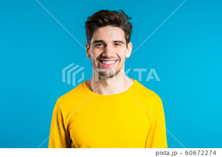 Handsome european man with trendy hairdo in yellow wear on blue studio background. Cheerful guy smiling and looking to camera. Handsome european man with trendy hairdo in yellow wear on blue studio background. Cheerful guy smiling and looking to camera. 60672274