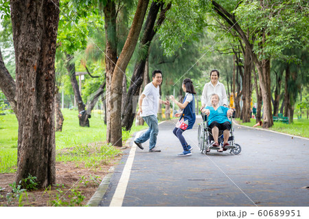 Happy family,asian little child girl or daughter playing touch,tag game,running with father,elderly woman in wheelchair,mother,senior grandmother having fun,laugh in outdoor park,parents enjoy vacatio 60689951