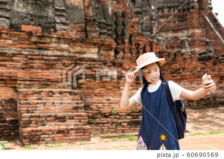Cute happy smiling tourist girl taking self-portrait picture with smartphone at Wat Chaiwatthanaram is a Buddhist temple in the city of Ayutthaya Historical Park,Thailand, summer vacation,travel conce 60690569