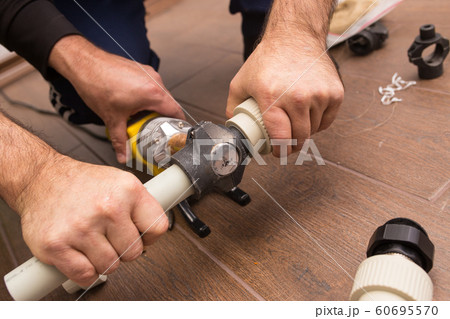 Soldering iron for a plastic water pipe close-up. Hands plumbers hold pipes. 60695570