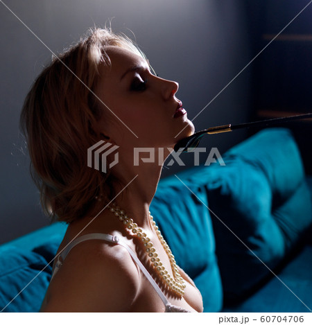 Blonde submissive woman with leather whip touches her chin. 60704706