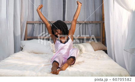 smiling African American lady wakes up and stretches on bed 60705582