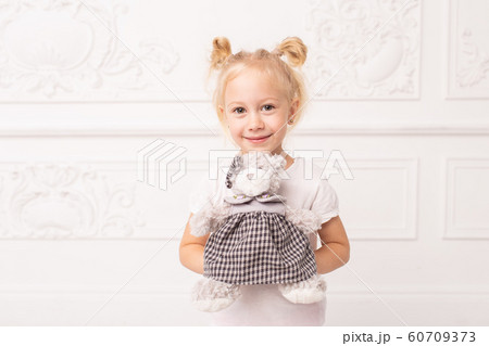 Little blond cheerful girl holds toy bear in hands and smile 60709373