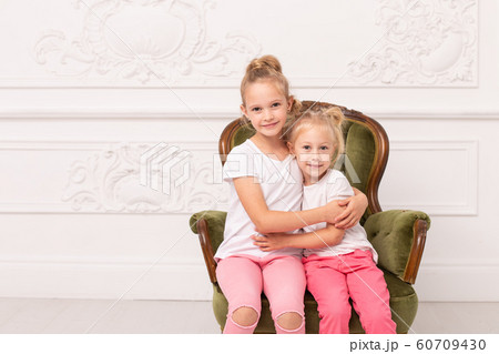 Two little blond sit in green armchair and hug each other 60709430