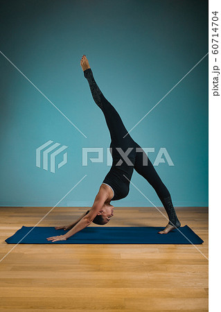 Sporty young woman doing stretching standing. Slim girl practicing yoga indoors on blue background. Calm, relax, healthy lifestyle concept. Sporty young woman doing stretching standing. Slim girl practicing yoga indoors on blue background. Calm, relax, healthy lifestyle concept. 60714704