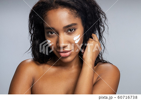 Calm attractive Afro American woman applying facial cream Calm attractive Afro American woman applying facial cream 60716738