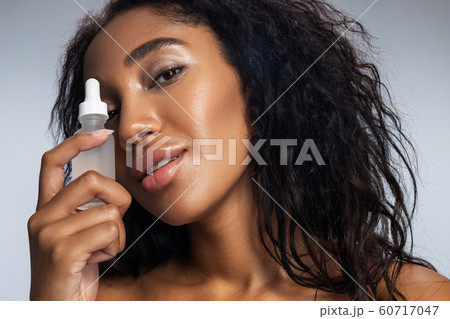 Afro American pretty woman with curly hair keeping bottle with cosmetic liquid 60717047