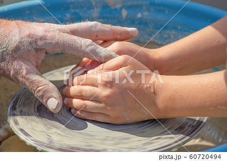 Hands of potter and child work with clay 60720494