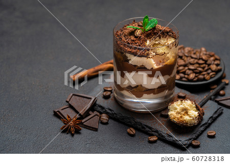 Classic tiramisu dessert in a glass cup and pieces of chocolate on stone cutting board on dark concrete background Classic tiramisu dessert in a glass cup and pieces of chocolate on stone cutting board on dark concrete background 60728318