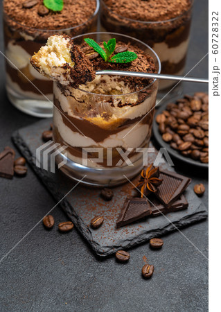 Classic tiramisu dessert in a glass cup and pieces of chocolate on stone cutting board on dark concrete background Classic tiramisu dessert in a glass cup and pieces of chocolate on stone cutting board on dark concrete background 60728322