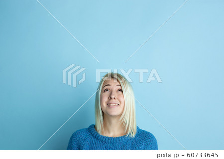 Portrait of young caucasian woman looks happy, dreamful on blue background 60733645