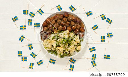 Traditional swedish meatballs (kottbullar) with cauliflower and green peas, brown sauce in the white plate. Swedish flags. Swedish national food concept. Background photo 60733709