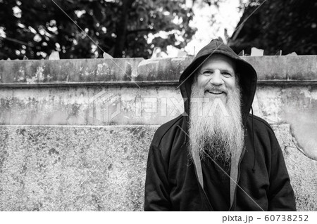 Happy mature bald man with long gray beard smiling against concrete wall outdoors 60738252