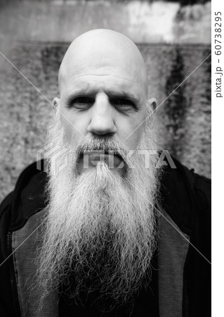 Face of mature bald man with long gray beard against concrete wall outdoors 60738295