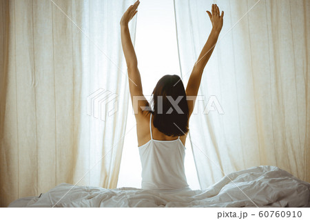 Woman stretching hands in bed after wake up, sun flare . Brunette entering a day happy and relaxed after good night sleep and back view. Concept of a new day and joyful weekend 60760910