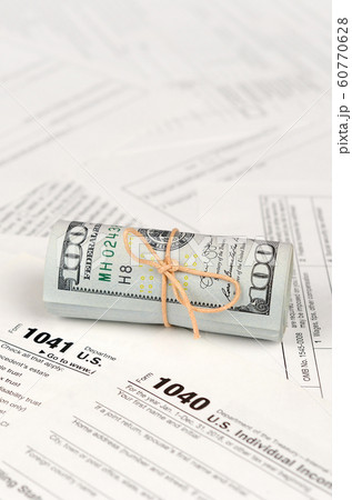 Tax forms lies near roll of hundred dollar bills. 60770628