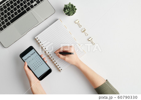 Hands of female employee holding smartphone and pen over blank page of notebook Hands of female employee holding smartphone and pen over blank page of notebook 60790330