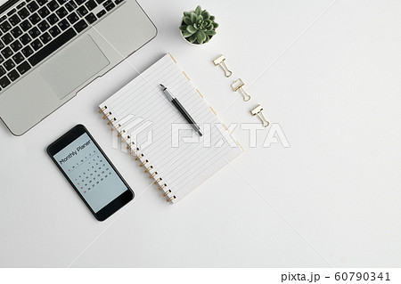 Notebook with pen, monthly planner in gadget, clips and other stuff on desk 60790341