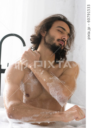 Young muscular man with closed eyes washing his body while having bath 60791533