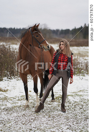 A beautiful girl in the red plaid shirt and pants rider walks with horse in early winter. space for text on white background 60797870