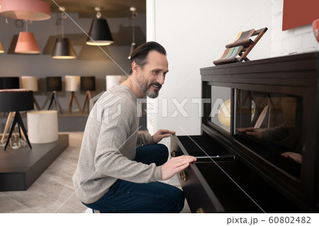 Dark-haired positive man touching the surface of furniture Dark-haired positive man touching the surface of furniture 60802482