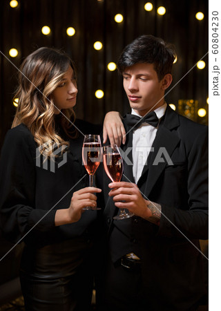 Elegant couple toasting the New Year with champagne and joy as they clink glasses against strings of twinkling party lights Elegant couple toasting the New Year with champagne and joy as they clink glasses against strings of twinkling party lights 60804230