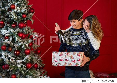 joyful couple celebrates Christmas. Glasses of champagne, gift in a box. Living room in bright christmas lights. joyful couple celebrates Christmas. Glasses of champagne, gift in a box. Living room in bright christmas lights. 60804256